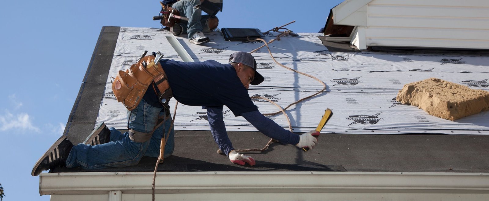 Roofing technician installing new asphalt shingles on a residential roof in daylight